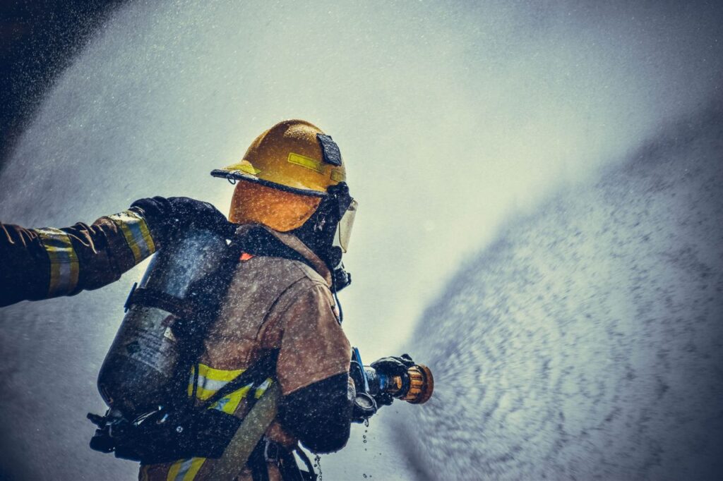 Photograph showing a brave firefighter in protective gear spraying water during training or emergency.